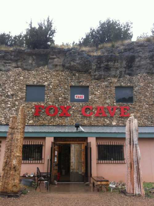 Entrance to Fox Cave, featuring a stone facade and large red letters, with two tall stone sculptures in front.