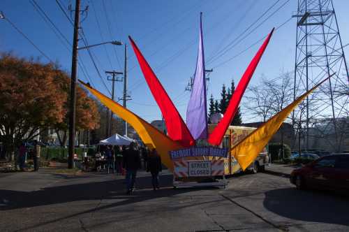 Colorful fabric banners in red, yellow, and purple mark the entrance to Fremont Sunday Market, with people walking in.