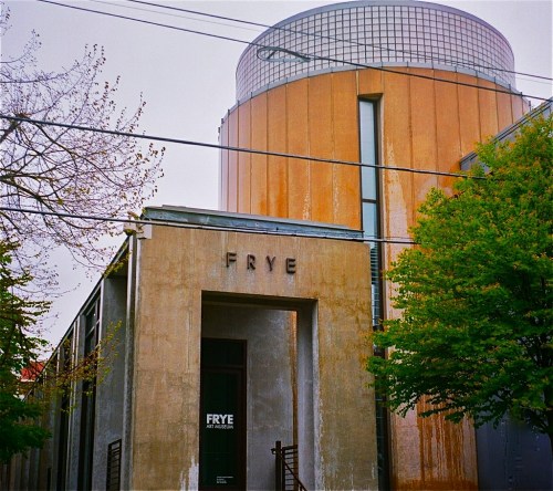 Modern building with "FRYE" signage, featuring a cylindrical top and surrounded by trees and power lines.