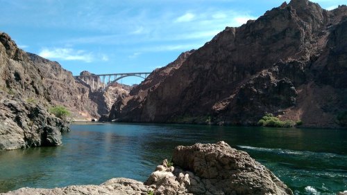 A scenic view of a river surrounded by rocky cliffs, with a bridge spanning across the landscape under a blue sky.