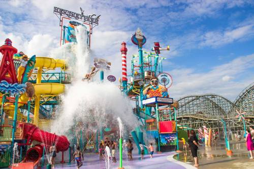 A vibrant water park with colorful slides, a large splash area, and people enjoying the attractions under a blue sky.