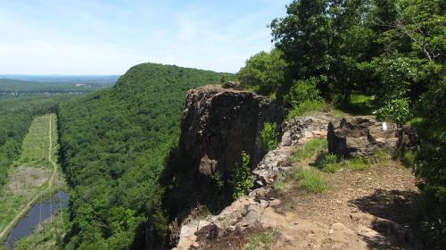 A scenic view from a rocky cliff overlooking lush green hills and a winding path below.