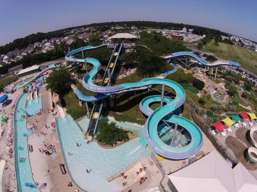 Aerial view of a water park featuring winding slides, a lazy river, and a pool area with sunbathers and umbrellas.