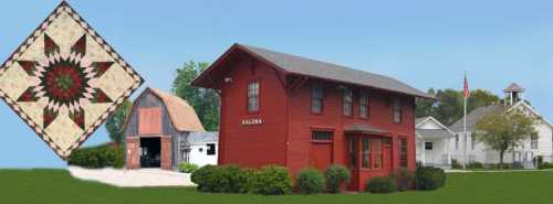 A red barn-style building with a quilt pattern in the corner, surrounded by greenery and a clear blue sky.