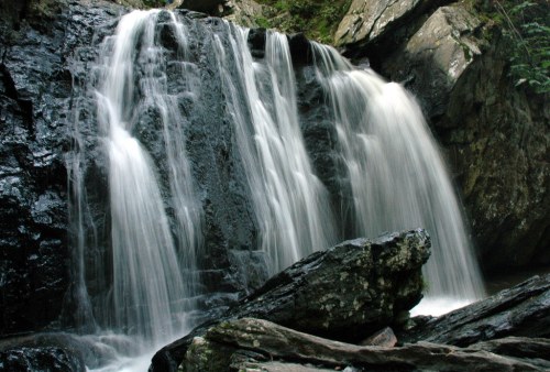 A serene waterfall cascading over dark rocks, surrounded by lush greenery.