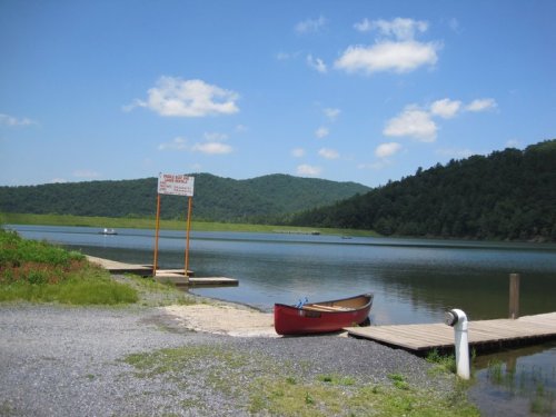 A serene lake scene with a red canoe by the dock, surrounded by green hills and a clear blue sky.