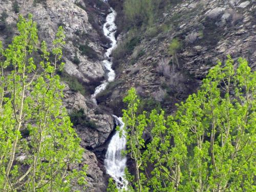A cascading waterfall flows through rocky terrain, surrounded by lush green foliage.