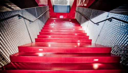 A vibrant red staircase with modern lighting, leading upward in a contemporary architectural space.