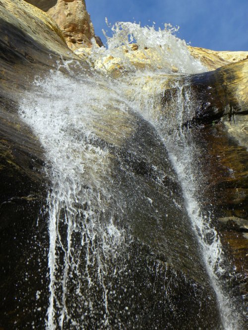 A close-up of a waterfall cascading over rocky terrain, with splashes of water against a blue sky.