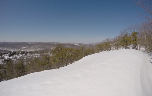 A snowy landscape with rolling hills and trees under a clear blue sky.