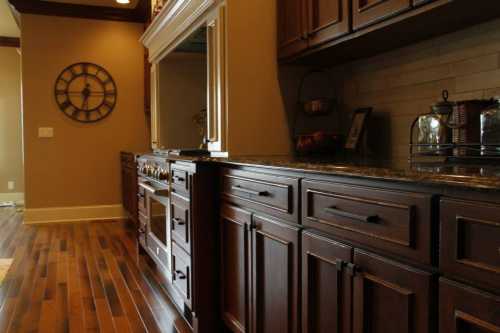 A modern kitchen with dark wooden cabinets, a granite countertop, and a wall clock, featuring hardwood flooring.