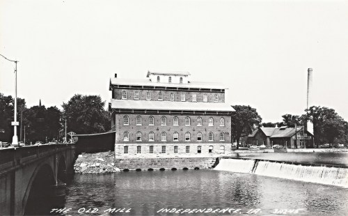 Historic black-and-white photo of The Old Mill in Independence, IA, beside a river and bridge.