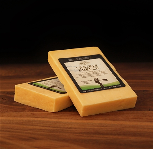 Two blocks of cheese with labels, resting on a wooden surface against a dark background.