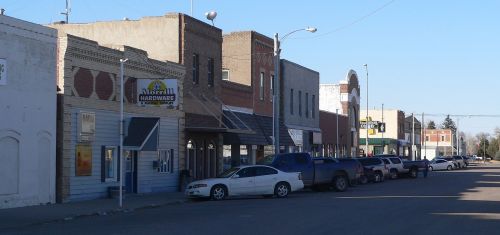 A quiet street lined with small businesses and parked cars in a small town.
