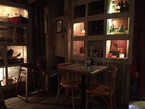 Cozy restaurant interior with wooden shelves, warm lighting, and a small table surrounded by chairs.