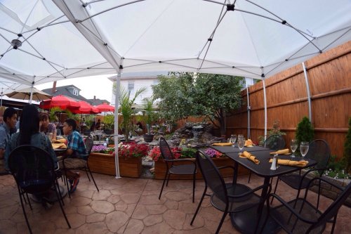 Outdoor dining area with tables under canopies, surrounded by greenery and flowers, creating a cozy atmosphere.