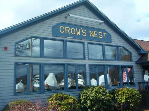 Exterior of a building named "Crow's Nest" with large windows showcasing boats and greenery in front.