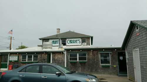 Aunt Carrie's restaurant exterior with a gray car parked in front, featuring a cloudy sky and American flag.