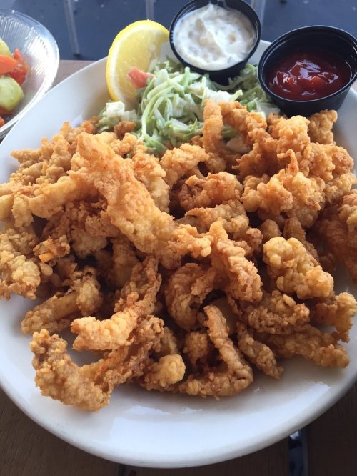 A plate of crispy fried calamari with lemon, coleslaw, and dipping sauces on the side.