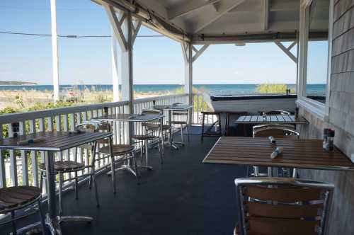 A seaside patio with empty tables and chairs, overlooking the ocean on a sunny day.