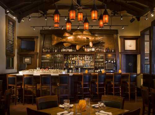 A cozy restaurant interior featuring a bar with a large fish sculpture, warm lighting, and wooden furniture.