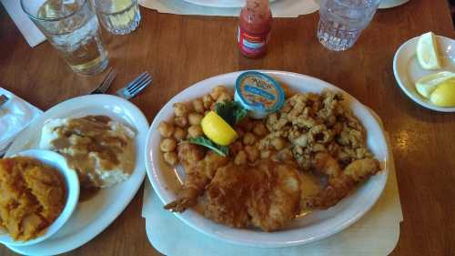 A plate of fried seafood with hushpuppies, coleslaw, and a side of mashed potatoes and sweet potatoes.