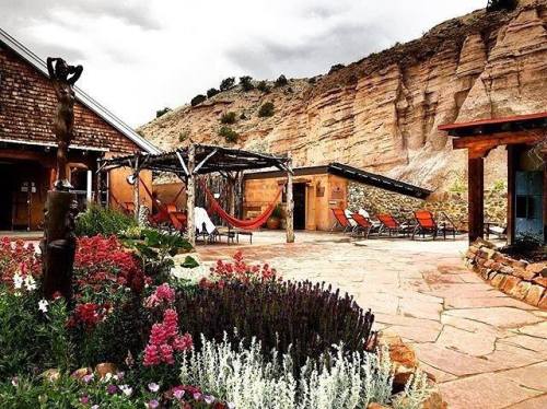 A serene outdoor space with colorful flowers, a hammock, and lounge chairs, set against a rocky hillside.