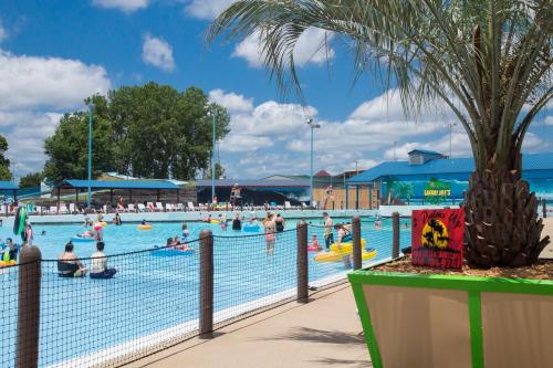 A vibrant pool scene with people swimming and floating, surrounded by palm trees and sunny skies.
