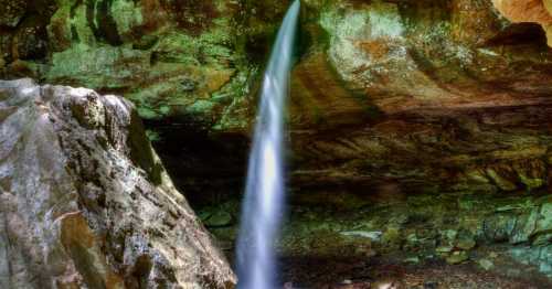 A serene waterfall cascades from a rocky overhang into a tranquil, moss-covered area below.