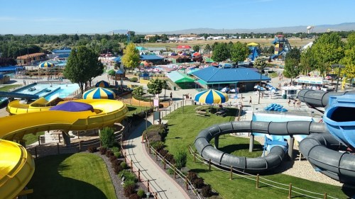 Aerial view of a vibrant water park featuring slides, pools, and colorful umbrellas, surrounded by greenery.