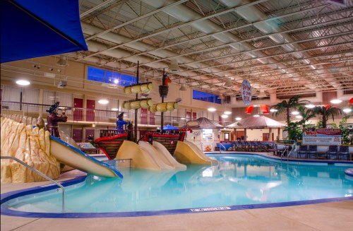 Indoor water park featuring a pirate ship, water slides, and palm trees around a large swimming pool.