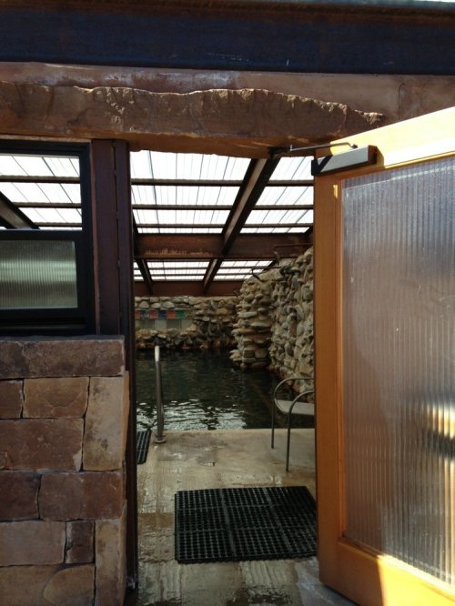 A doorway opens to a serene indoor pool area with stone walls and a glass roof, inviting relaxation.