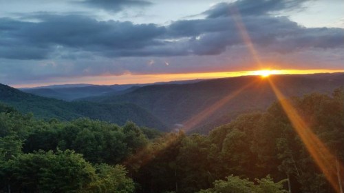 A scenic view of mountains at sunset, with vibrant colors and rays of sunlight breaking through the clouds.