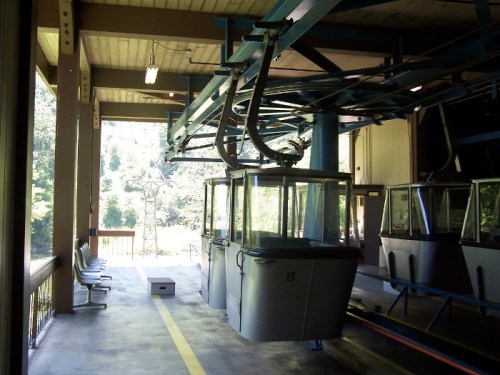 A cable car station with empty cabins and seating area, surrounded by trees and natural scenery.