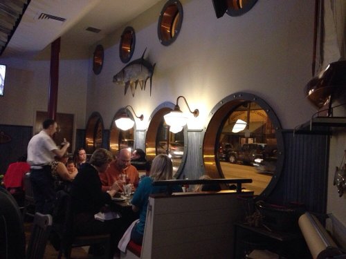 A cozy restaurant interior with round windows, a fish decoration, and diners enjoying their meals at a table.