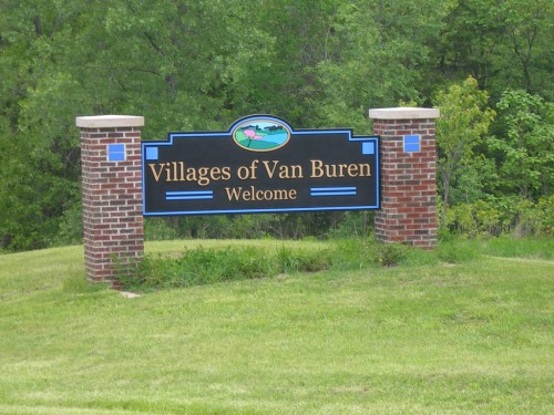 Sign welcoming visitors to the Villages of Van Buren, surrounded by greenery and grass.