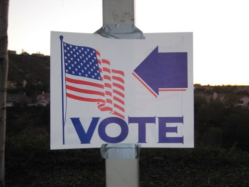 Sign directing voters with an American flag and an arrow pointing left, encouraging people to vote.