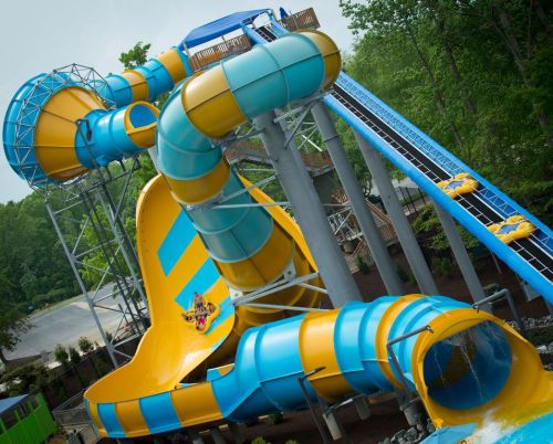 A colorful water slide with twisting tubes and a large splash pool at the bottom, surrounded by trees.