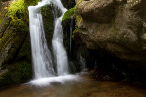 A serene waterfall cascading over moss-covered rocks into a calm pool below.