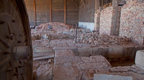 Interior of an old building with stone foundations, brick walls, and piles of stones, showcasing historical architecture.