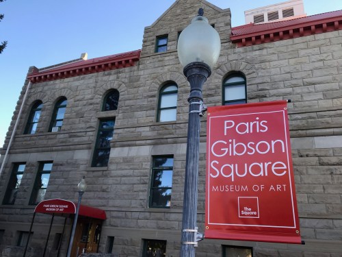 Sign for Paris Gibson Square Museum of Art in front of a historic stone building with a clear blue sky.