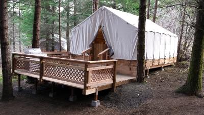 A wooden platform with a tent-like structure surrounded by trees, featuring a deck and steps leading to the entrance.