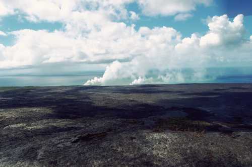 A vast, barren landscape with volcanic smoke rising against a backdrop of blue sky and fluffy clouds.