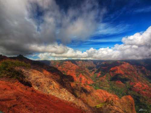 A vibrant landscape of red and green canyons under a dramatic sky with clouds.