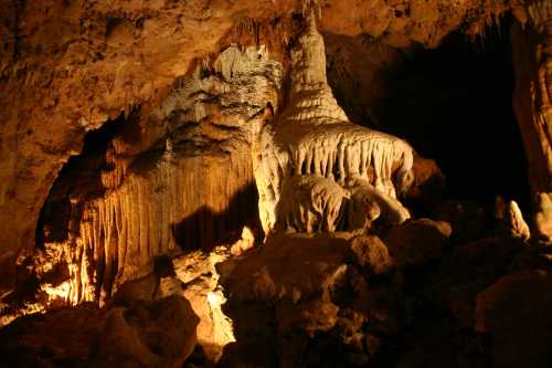 Stalactites and stalagmites illuminated in a dark cave, showcasing intricate rock formations and textures.