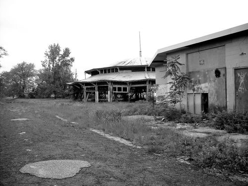 Abandoned buildings with overgrown grass and a cracked path, captured in black and white.
