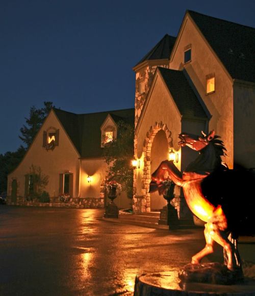 A beautifully lit house at night with a horse statue in the foreground, showcasing elegant architecture and a serene atmosphere.