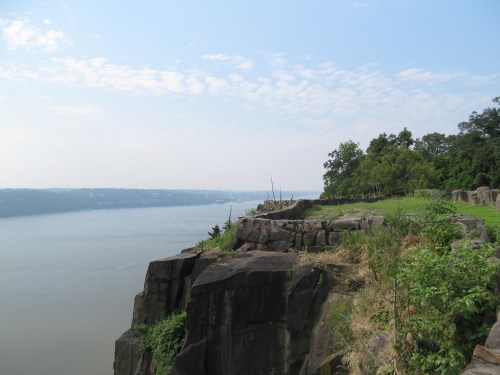 A scenic view of a river from a rocky cliff, surrounded by greenery and a clear blue sky.