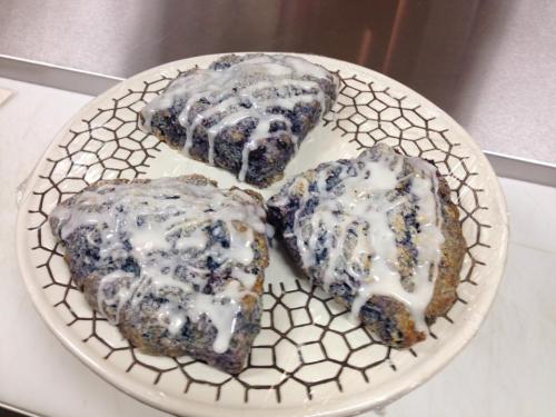 Three blueberry scones drizzled with icing on a decorative plate.