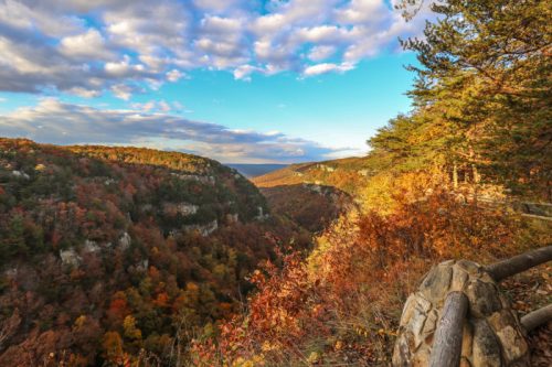 A scenic view of a colorful autumn landscape with rolling hills, trees, and a blue sky dotted with clouds.